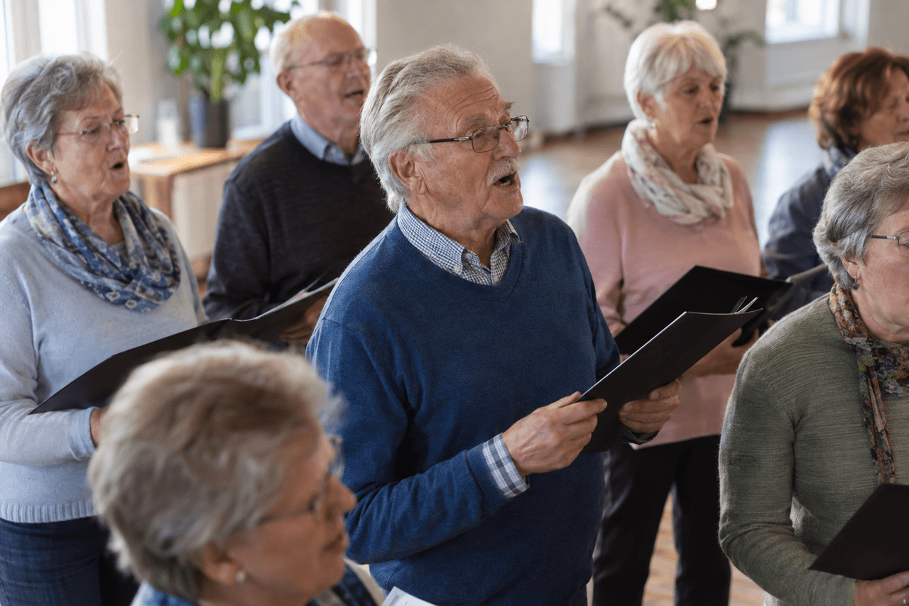 Älterer Mann singt mit anderen Seniorinnen und Senioren in einem Chor in einem hellen Saal